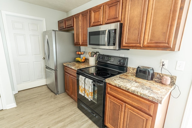 kitchen featuring light wood-type flooring, a textured ceiling, light stone countertops, and stainless steel appliances