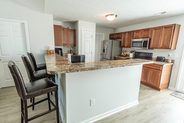 kitchen featuring kitchen peninsula, light hardwood / wood-style flooring, appliances with stainless steel finishes, a kitchen breakfast bar, and light stone countertops