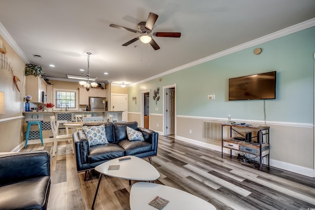 living room with ornamental molding, ceiling fan with notable chandelier, and hardwood / wood-style floors