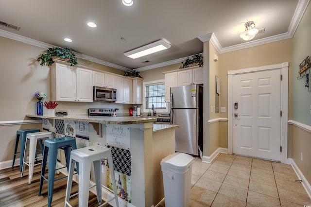 kitchen with white cabinets, kitchen peninsula, a breakfast bar area, stainless steel appliances, and crown molding