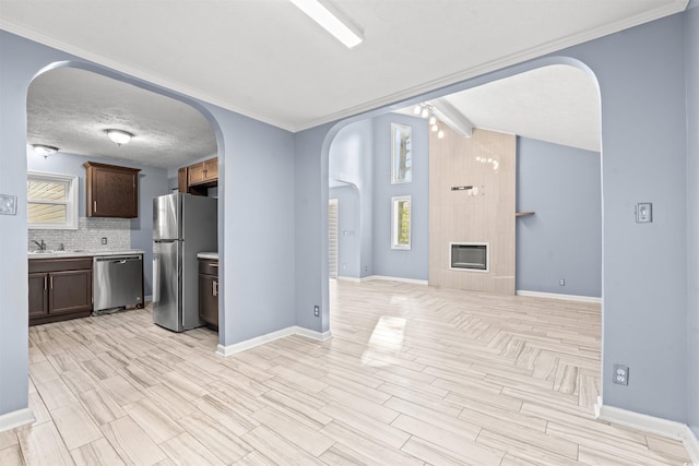 kitchen with appliances with stainless steel finishes, backsplash, a fireplace, light wood-type flooring, and ornamental molding