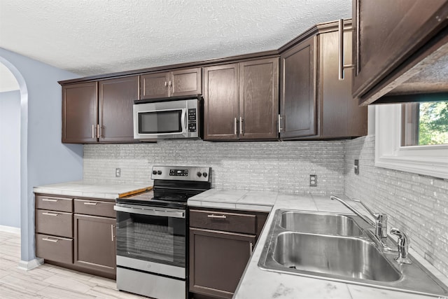 kitchen featuring dark brown cabinets, backsplash, appliances with stainless steel finishes, and sink