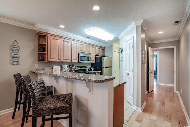 kitchen featuring a breakfast bar, a peninsula, stainless steel appliances, light wood-style flooring, and light stone counters