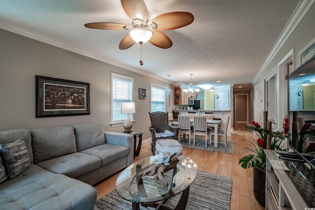 living area featuring baseboards, ornamental molding, a textured ceiling, light wood finished floors, and ceiling fan with notable chandelier