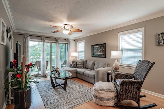 living room featuring light wood-style floors, a textured ceiling, crown molding, and ceiling fan