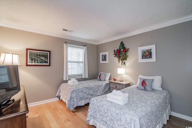 bedroom with wood finished floors, baseboards, ornamental molding, and visible vents
