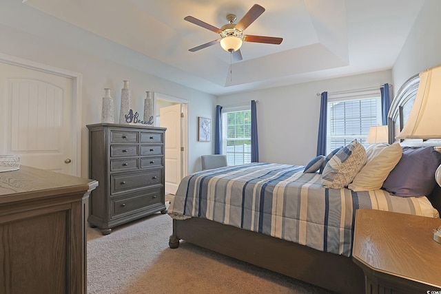 bedroom with light carpet, ceiling fan, and a raised ceiling