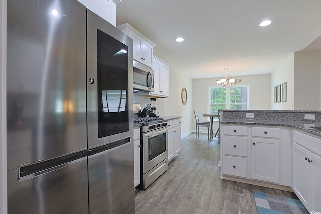 kitchen with appliances with stainless steel finishes, white cabinetry, light hardwood / wood-style flooring, dark stone counters, and a notable chandelier