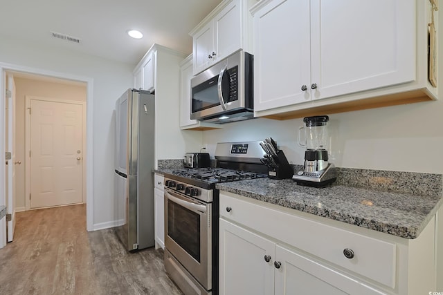 kitchen with dark stone counters, light wood-type flooring, white cabinetry, and appliances with stainless steel finishes