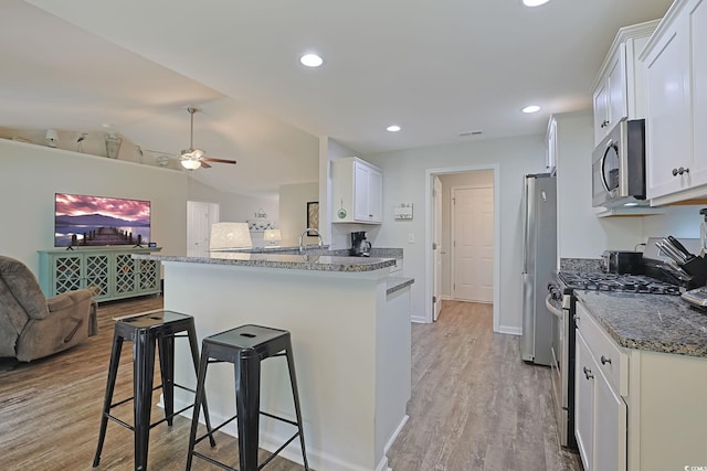 kitchen with ceiling fan, kitchen peninsula, white cabinetry, appliances with stainless steel finishes, and a breakfast bar