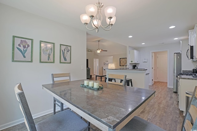 dining space featuring ceiling fan with notable chandelier, light wood-type flooring, and sink