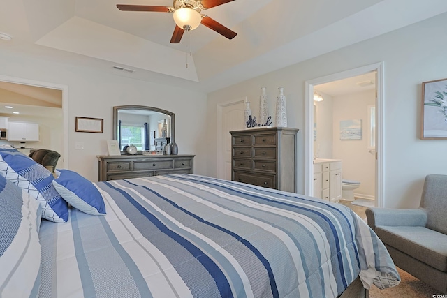 bedroom featuring a tray ceiling, ensuite bath, and ceiling fan