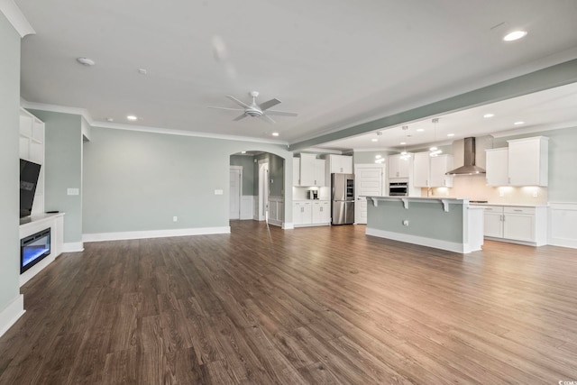 unfurnished living room with ceiling fan, crown molding, arched walkways, wood finished floors, and recessed lighting