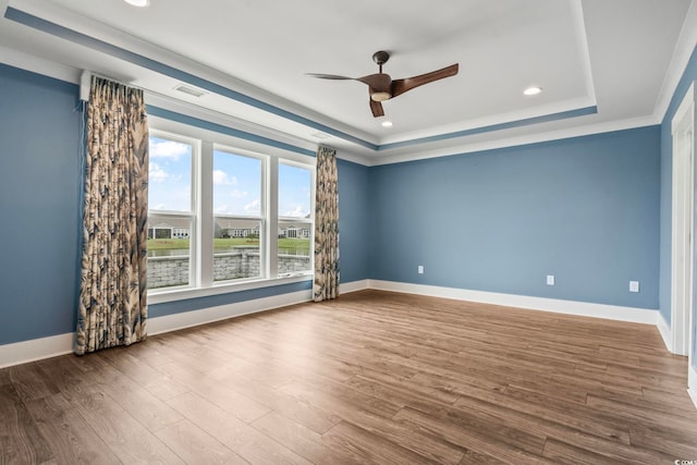 spare room with wood-type flooring, crown molding, ceiling fan, and a raised ceiling