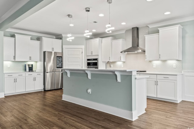 kitchen featuring hardwood / wood-style flooring, appliances with stainless steel finishes, hanging light fixtures, and wall chimney range hood