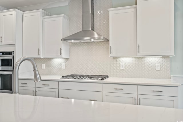 kitchen featuring light countertops, stainless steel appliances, wall chimney exhaust hood, and white cabinetry