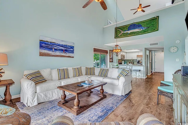 living room with ceiling fan with notable chandelier, light hardwood / wood-style flooring, and high vaulted ceiling