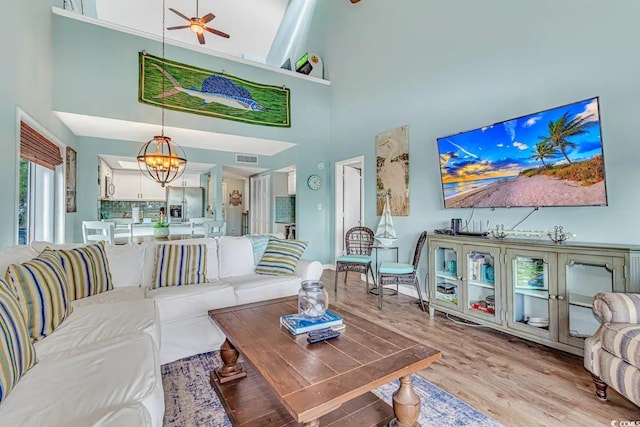 living room featuring light wood-type flooring, ceiling fan with notable chandelier, and a towering ceiling