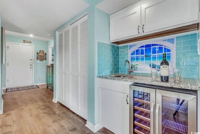 bar with sink, beverage cooler, backsplash, white cabinetry, and light hardwood / wood-style floors