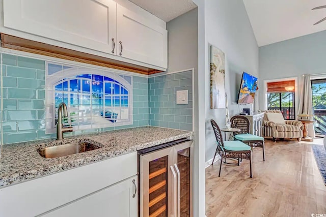 kitchen featuring light wood-type flooring, wine cooler, tasteful backsplash, sink, and white cabinets