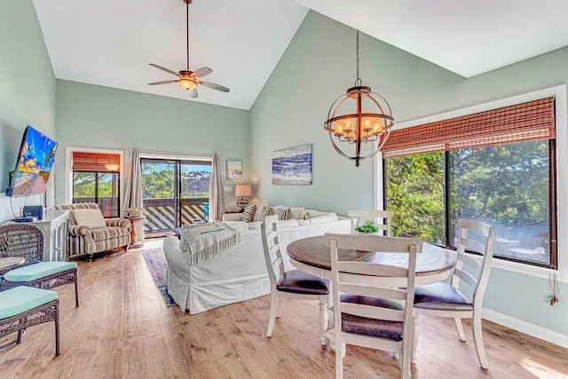 dining room with ceiling fan with notable chandelier, light hardwood / wood-style flooring, and high vaulted ceiling