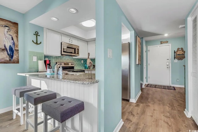 kitchen with appliances with stainless steel finishes, kitchen peninsula, white cabinetry, and a kitchen breakfast bar