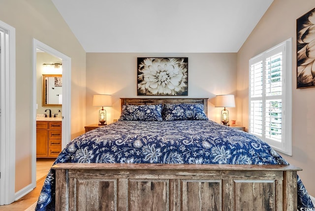 bedroom featuring light wood-type flooring, connected bathroom, vaulted ceiling, and sink