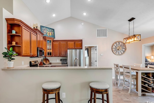 kitchen featuring vaulted ceiling, kitchen peninsula, pendant lighting, stainless steel appliances, and light hardwood / wood-style flooring