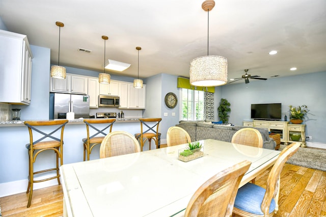 dining area featuring ceiling fan, light hardwood / wood-style flooring, and a fireplace