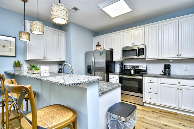 4808 Cantor Ct, North Myrtle Beach, SC 29582 - kitchen featuring stainless steel appliances, a kitchen breakfast bar, a peninsula, light stone countertops, and white cabinets