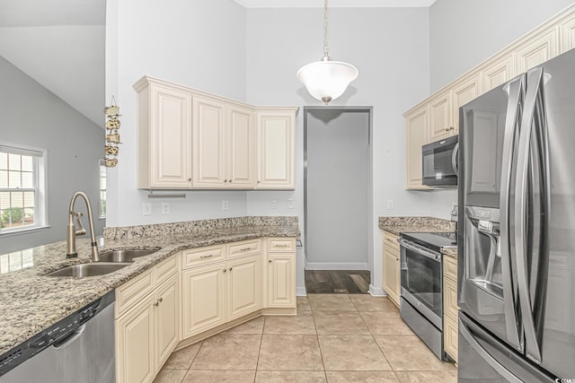 kitchen with sink, hanging light fixtures, cream cabinetry, light stone counters, and stainless steel appliances