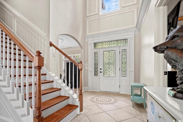 entrance foyer featuring crown molding, a high ceiling, light tile patterned flooring, and plenty of natural light