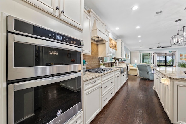 kitchen featuring pendant lighting, dark hardwood / wood-style floors, ceiling fan with notable chandelier, decorative backsplash, and appliances with stainless steel finishes