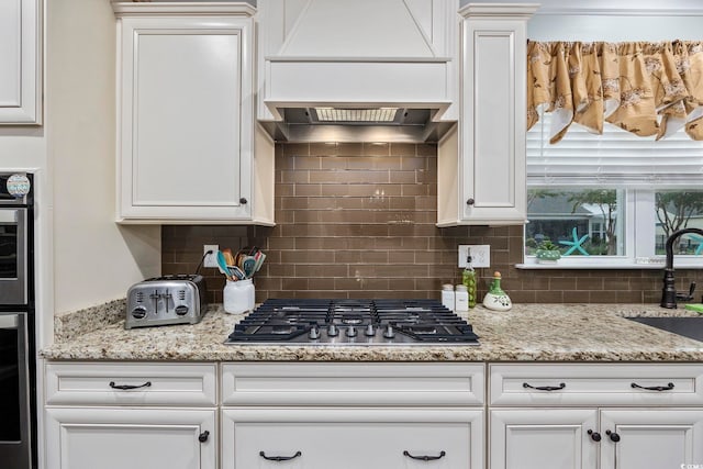 kitchen featuring white cabinets, light stone countertops, custom range hood, and tasteful backsplash