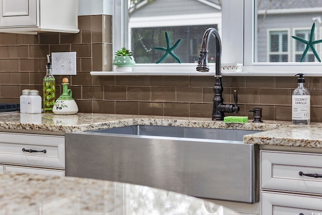 kitchen with decorative backsplash, sink, light stone counters, and white cabinets