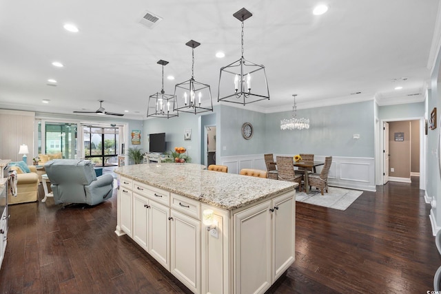 kitchen featuring hanging light fixtures, a kitchen island, ornamental molding, ceiling fan, and light stone countertops