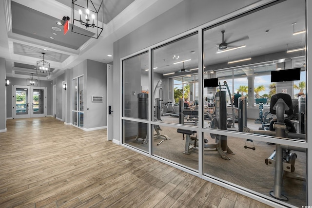 exercise room with french doors, ceiling fan with notable chandelier, and hardwood / wood-style floors