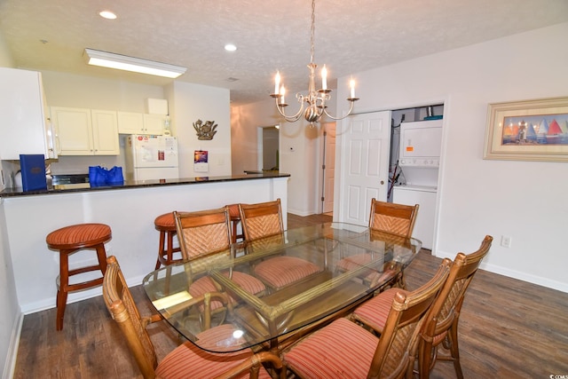 dining area with stacked washer / drying machine, a textured ceiling, an inviting chandelier, and dark hardwood / wood-style flooring