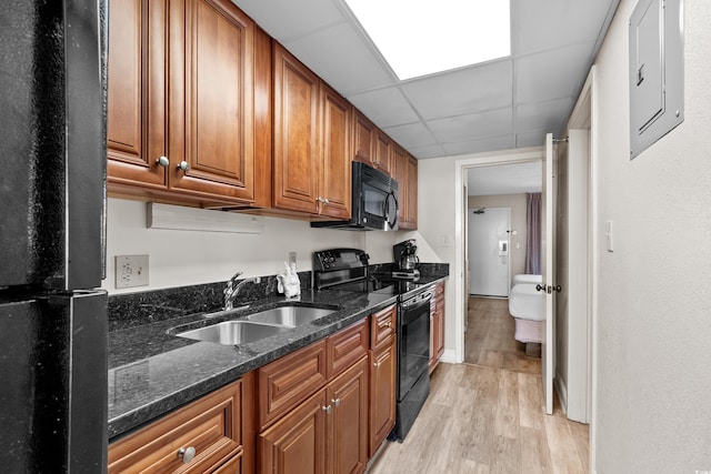 kitchen featuring sink, black appliances, a drop ceiling, dark stone countertops, and light wood-type flooring