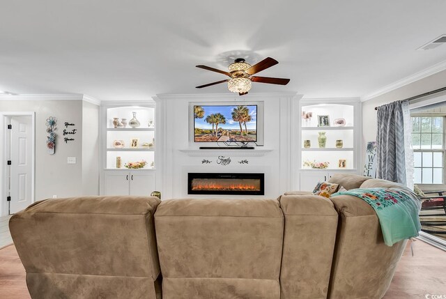 living room featuring light wood-type flooring, ceiling fan, built in shelves, and crown molding