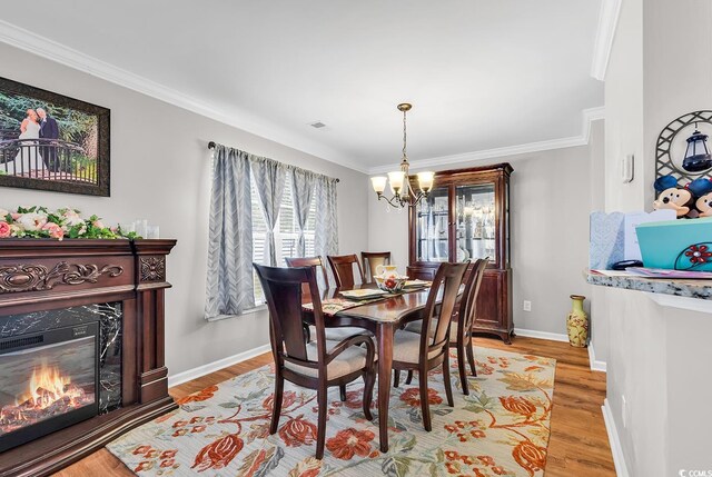 dining area featuring ornamental molding, light hardwood / wood-style floors, a fireplace, and a chandelier