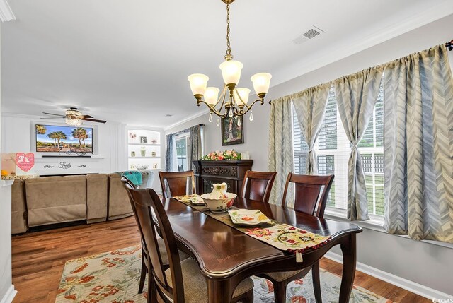 dining space with ceiling fan with notable chandelier, wood-type flooring, and ornamental molding