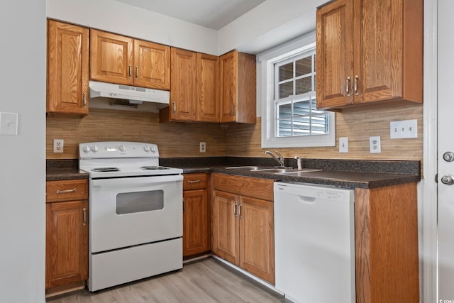 kitchen featuring white appliances, dark countertops, brown cabinets, under cabinet range hood, and a sink