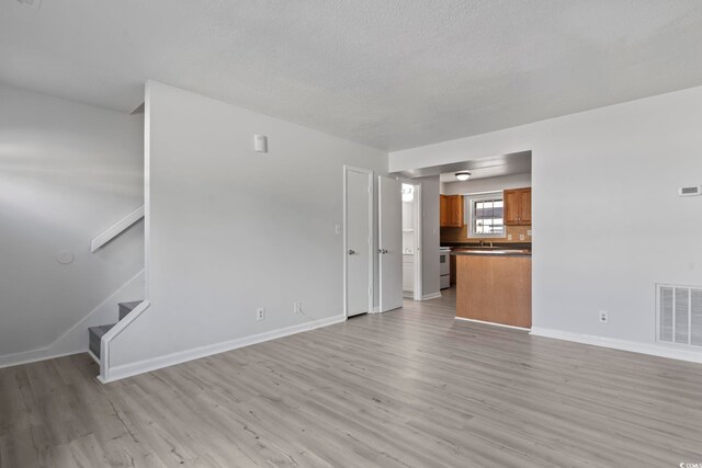 unfurnished living room with light wood-style floors, baseboards, stairs, and visible vents