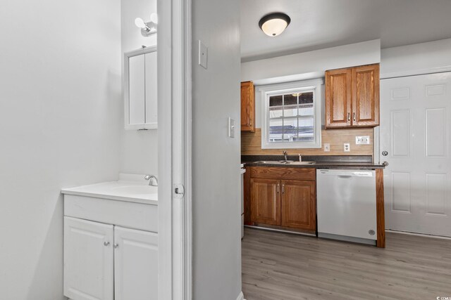 kitchen featuring light wood finished floors, tasteful backsplash, dishwasher, brown cabinets, and a sink