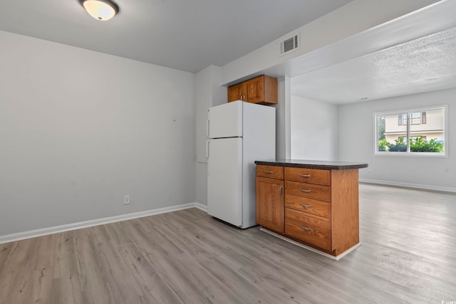 kitchen with baseboards, visible vents, dark countertops, brown cabinets, and freestanding refrigerator