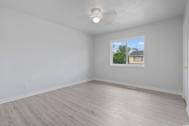 empty room with light wood-style floors, visible vents, baseboards, and a textured ceiling