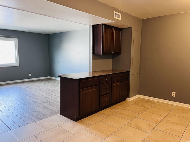 kitchen with light tile patterned floors, baseboards, visible vents, a peninsula, and dark brown cabinets