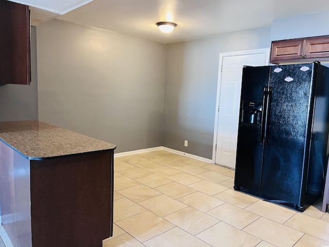 kitchen with dark stone counters, light tile patterned flooring, black fridge with ice dispenser, and baseboards