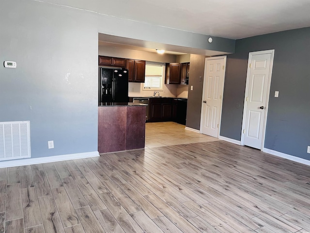 kitchen featuring light wood-style flooring, black fridge with ice dispenser, visible vents, and baseboards